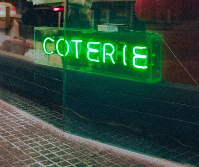 A green Coterie neon sign glowing in a storefront window.