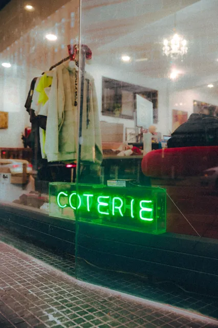 A green Coterie neon sign glowing in a storefront window.