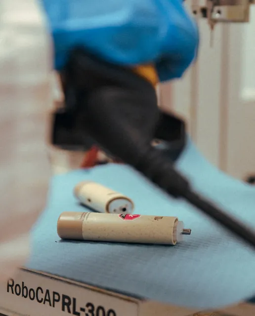 A close-up of a gloved hand handling a pre-roll at a workbench.