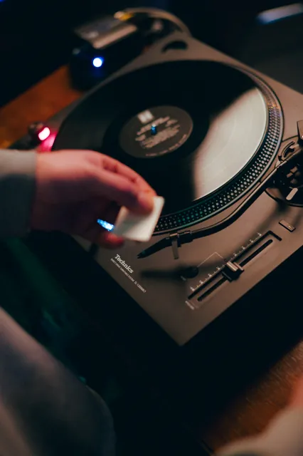 A hand cueing a vinyl record on a turntable.