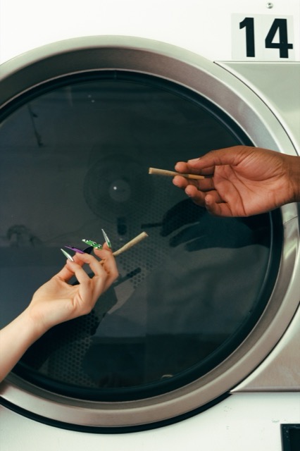 Two hands holding pre-rolls in front of a circular washing-machine door numbered fourteen.