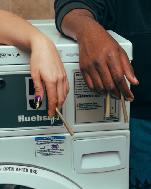 Two hands holding pre-rolls beside washing-machine controls.