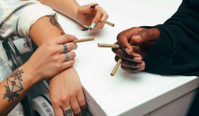 A close view of hands holding pre-rolls over a white surface.