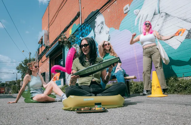 Three people posing outside a mural-covered storefront with Coterie products.