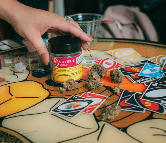 A hand reaching for a Coterie jar on a table covered in graphic stickers.
