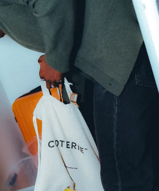 A person carrying a cream Coterie tote bag outdoors.