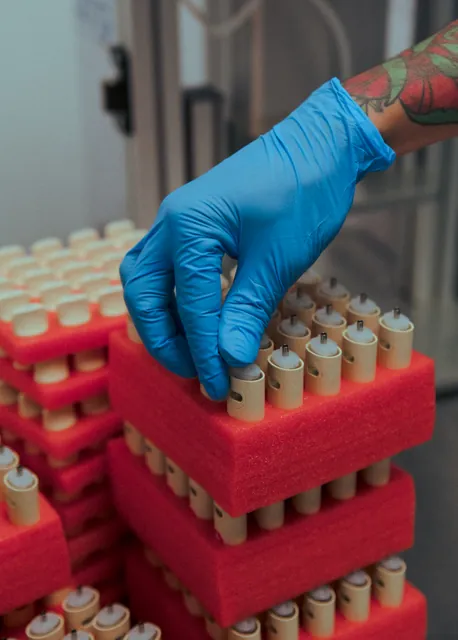 A gloved hand arranging Coterie pre-roll tubes in a red packing tray.