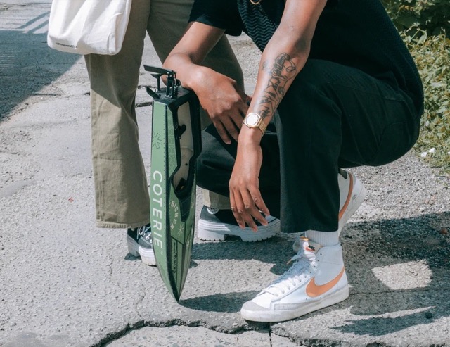 Hands, sneakers and a green Coterie prop on a sunny street.